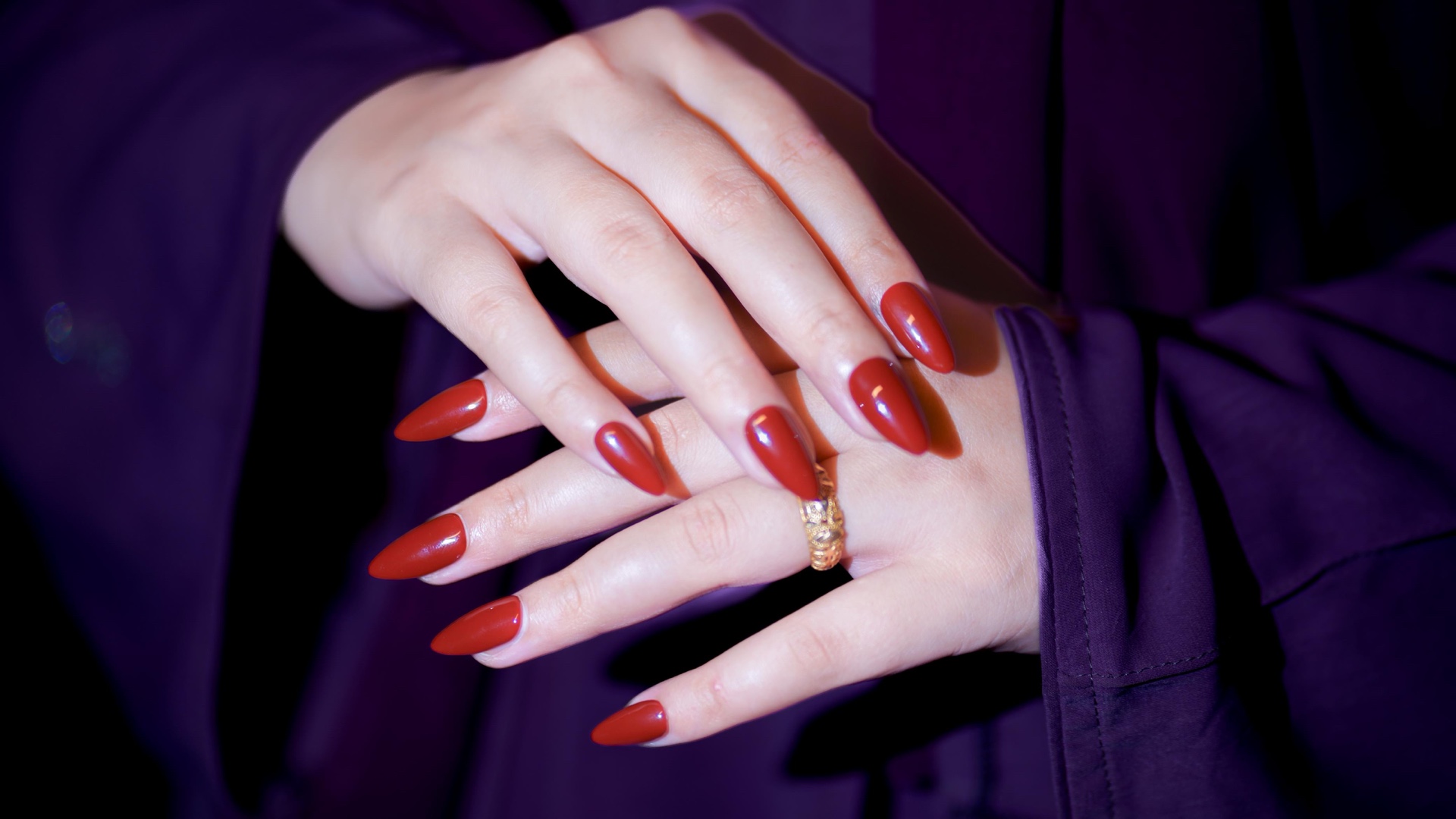 Matte deep-red almond press-on gel nails on both hands against a draped purple silk backdrop — handmade by Nails by Mona in Mirpur